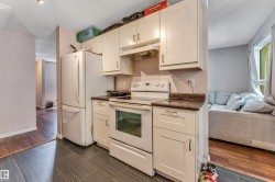 Kitchen featuring white cabinetry with brushed nickel hardware, a white electric range with overhead hood, a white refrigerator, and dark wood-finish countertops - 