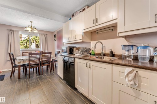 Kitchen area featuring cream cabinetry, stainless steel sink, and black appliances, complemented by dark wood-finish flooring - 24 1651 46 Street, Edmonton, AB 