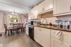 Kitchen area featuring cream cabinetry, stainless steel sink, and black appliances, complemented by dark wood-finish flooring - 