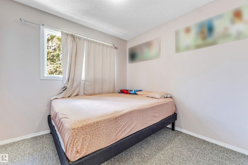 Bedroom featuring a window with exterior tree scenery, light-colored walls, and textured carpeting - 24 1651 46 Street, Edmonton, AB 