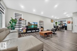 Open-concept living area featuring wood-finish flooring, recessed lighting, and large windows with blinds - 