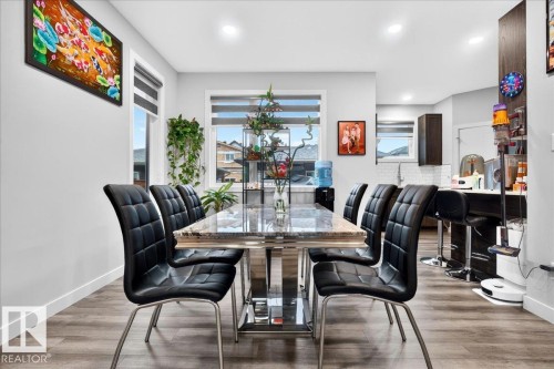 Open-concept dining area featuring wood-finish flooring, a contemporary dining table with a stone-finish top, and recessed ceiling lighting - 18139 75 Street, Edmonton, AB 
