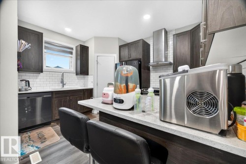 Modern kitchen featuring dark wood-finish cabinetry, white subway tile backsplash, stainless steel appliances, a stainless steel range hood, and light-toned countertops - 18139 75 Street, Edmonton, AB 