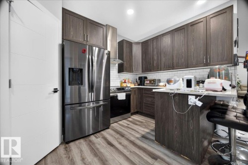 Modern kitchen featuring dark wood-finish cabinetry, stainless steel appliances, light countertops, a subway tile backsplash, and wood-finish flooring - 18139 75 Street, Edmonton, AB 