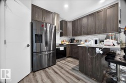 Modern kitchen featuring dark wood-finish cabinetry, stainless steel appliances, light countertops, a subway tile backsplash, and wood-finish flooring - 