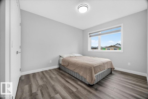 Bedroom featuring wood-finish flooring, a contemporary ceiling light fixture, white trim, and a window with roller shades - 18139 75 Street, Edmonton, AB 