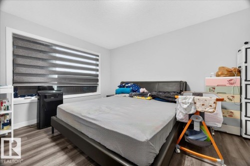 Bedroom featuring a large window with layered blinds, wood-finish flooring, and light gray wall paint - 18139 75 Street, Edmonton, AB 