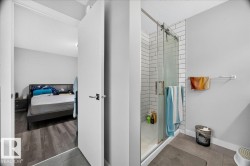 Glass-enclosed shower with white subway tile surround, matte gray wall paint, and wood-finish flooring extending into the adjoining room - 