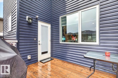 Exterior featuring dark blue horizontal siding, a light wood-finish deck, and a white framed door - 18139 75 Street, Edmonton, AB 