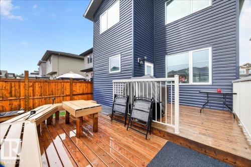 Expansive wood-finish deck with white railing, featuring dark blue horizontal siding, white trim windows, and a wood privacy fence - 18139 75 Street, Edmonton, AB 