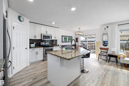 Kitchen featuring white cabinetry, stainless steel appliances, a center island with a stone countertop and seating, and wood-finish flooring - 25 Halladay Boulevard, Spruce Grove, AB - Indoor Photo Showing Kitchen With Double Sink