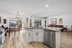 Open-concept kitchen featuring an island with granite countertops, white shaker cabinetry, and stainless steel appliances - 