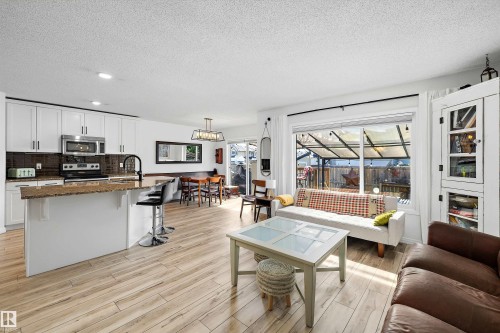 Open-concept living space featuring wood-finish flooring, a white kitchen island with bar seating, and white cabinetry - 25 Halladay Boulevard, Spruce Grove, AB - Indoor