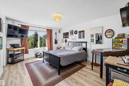 Bedroom featuring wood-finish flooring, a contemporary ceiling light fixture, and a window with extensive tree coverage visible - 25 Halladay Boulevard, Spruce Grove, AB - Indoor Photo Showing Bedroom