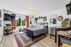 Bedroom featuring wood-finish flooring, a contemporary ceiling light fixture, and a window with extensive tree coverage visible - 