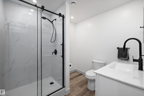 Modern bathroom featuring a glass-enclosed shower with matte black fixtures, large format white tile walls, a white vanity with an integrated sink, and wood-finish flooring - 25 Halladay Boulevard, Spruce Grove, AB - Indoor Photo Showing Bathroom