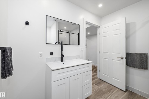 Bathroom featuring a white shaker vanity with a single sink, black hardware, framed mirror, and wood-finish flooring - 25 Halladay Boulevard, Spruce Grove, AB - Indoor