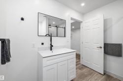 Bathroom featuring a white shaker vanity with a single sink, black hardware, framed mirror, and wood-finish flooring - 