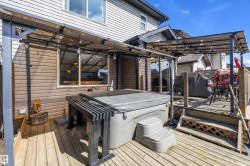 Expansive wooden deck featuring a hot tub, a built-in outdoor bar, and a covered patio area with string lights - 