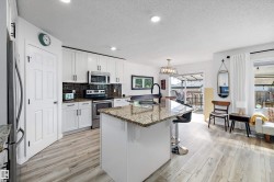 Kitchen featuring white cabinetry, stainless steel appliances, a center island with a stone countertop and seating, and wood-finish flooring - 