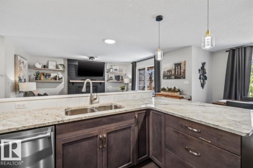 Kitchen island featuring light-toned countertops, a double basin stainless steel sink with a gooseneck faucet, and dark wood-finish cabinetry - 14 Edinburgh Crt N, St. Albert, AB 