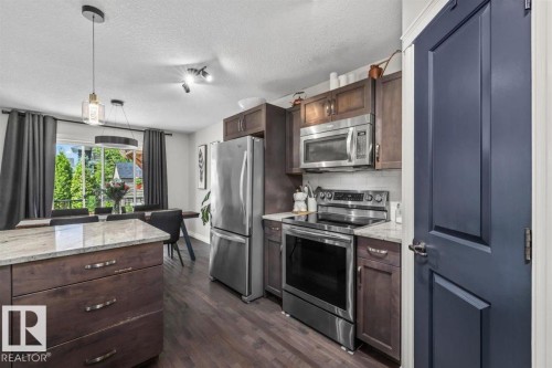 Kitchen featuring stainless steel appliances, wood-finish flooring, a spacious island with a light-toned countertop, dark wood cabinetry, and a bright window looking out to trees - 14 Edinburgh Crt N, St. Albert, AB 