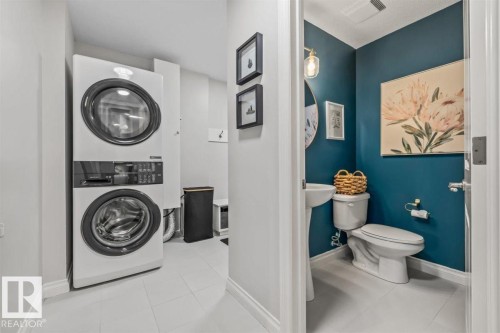 Dedicated laundry area featuring a stacked washer and dryer, complemented by a nearby half bath with a pedestal sink and wall-mounted light fixture - 14 Edinburgh Crt N, St. Albert, AB 