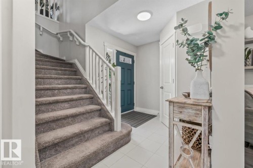 Entryway featuring a carpeted staircase with white railings, a teal front door with decorative glass, and light tile flooring - 14 Edinburgh Crt N, St. Albert, AB 