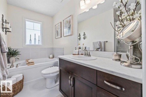 Bathroom featuring a built-in tub with tile surround, a window above the tub, a dark wood-finish vanity with a white countertop, and an integrated sink with a chrome faucet - 14 Edinburgh Crt N, St. Albert, AB 