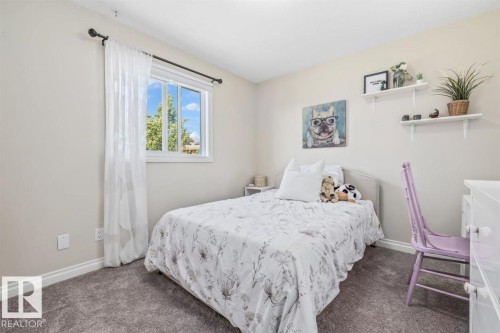 Bright bedroom featuring a large window, soft neutral wall tones, plush gray carpet, white baseboards, and built-in white floating shelves - 14 Edinburgh Crt N, St. Albert, AB 