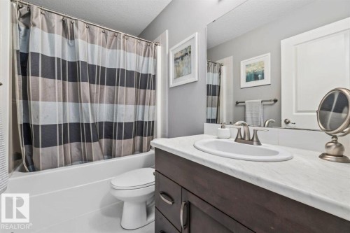 Bathroom featuring a dark wood-finish vanity with a white countertop and an integrated sink, brushed nickel faucet, large wall-mounted mirror, and a white bathtub with an overhead shower - 14 Edinburgh Crt N, St. Albert, AB 