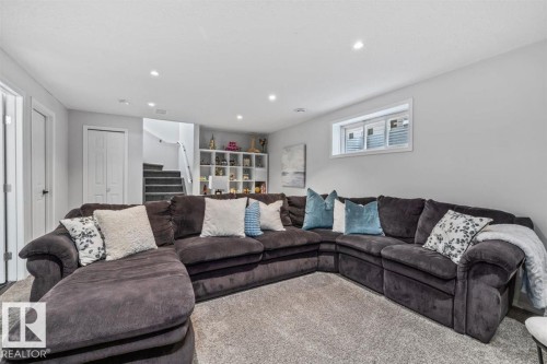 Spacious recreation area featuring plush carpeting, recessed ceiling lighting, a built-in shelving unit, a window, and a staircase with a white railing - 14 Edinburgh Crt N, St. Albert, AB 