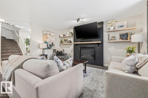 Living area featuring a black shiplap fireplace with a wood mantel, built-in shelving, and carpeted stairs with white railings - 14 Edinburgh Crt N, St. Albert, AB 