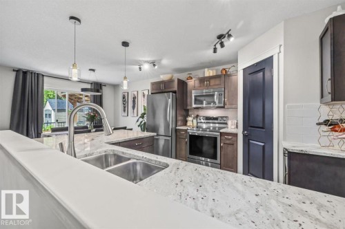 Kitchen featuring white speckled countertops, stainless steel dual basin sink with gooseneck faucet, dark wood-finish cabinetry, and stainless steel appliances - 14 Edinburgh Crt N, St. Albert, AB 