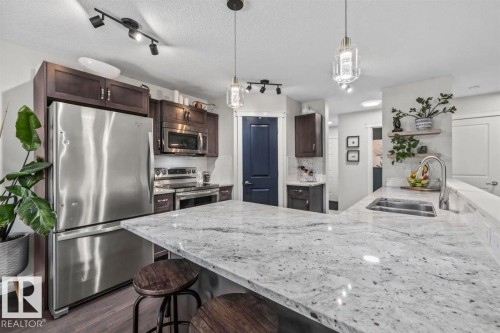 Spacious kitchen featuring an extended white granite countertop with an undermount sink, stainless steel appliances, dark wood cabinetry, and wood-finish flooring - 14 Edinburgh Crt N, St. Albert, AB 