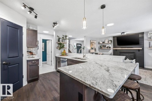 Open-concept kitchen featuring an expansive island with a light-toned countertop, stainless steel appliances, and wood-finish flooring - 14 Edinburgh Crt N, St. Albert, AB 