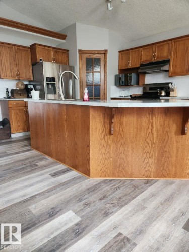 Kitchen featuring wood cabinetry, stainless steel appliances, and a central island with a white countertop - 49 Heritage Drive, St. Albert, AB 