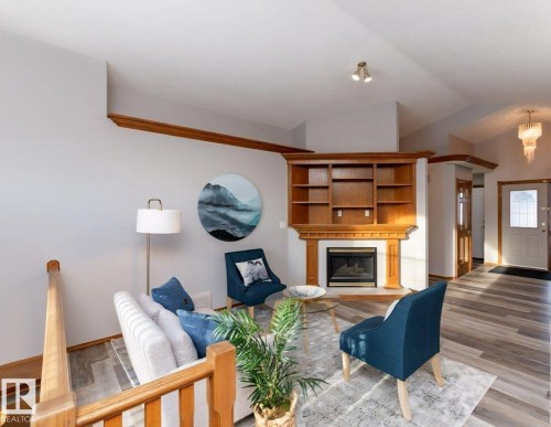 Living area featuring a fireplace with built-in wooden shelving, vaulted ceilings, and wood-finish flooring - 49 Heritage Drive, St. Albert, AB 