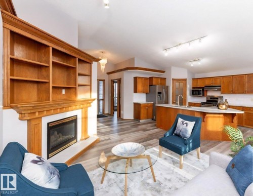 Vaulted ceiling living area featuring a built-in wood fireplace with integrated shelving, wood-finish flooring, and track lighting - 49 Heritage Drive, St. Albert, AB 
