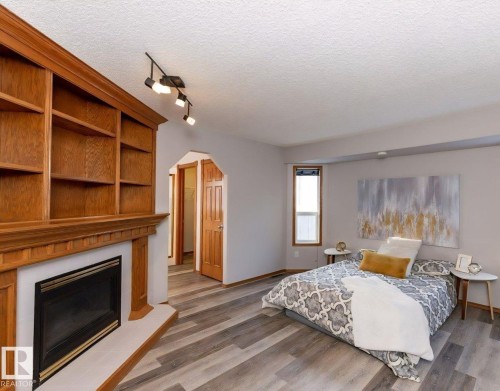 Integrated wood-finish shelving surrounding a fireplace with a white hearth, complemented by wood-finish flooring, a window with wood-finish trim, and track lighting - 49 Heritage Drive, St. Albert, AB 