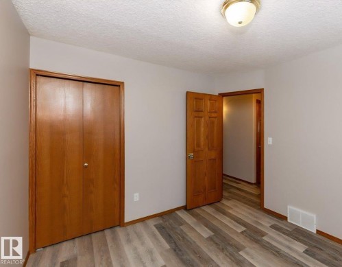 Interior room featuring wood-finish flooring, neutral wall paint, and a textured ceiling - 49 Heritage Drive, St. Albert, AB 