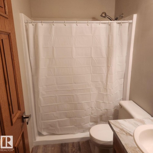 Full bathroom featuring a white shower surround with a brushed nickel showerhead, a white toilet, and a vanity with a white basin sink and a faux-marble countertop - 49 Heritage Drive, St. Albert, AB 