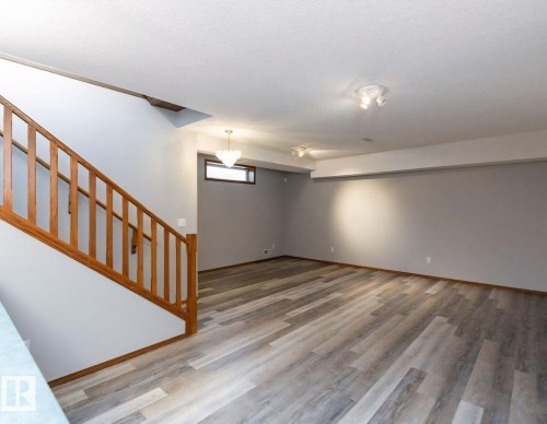 Spacious room featuring wood-finish flooring, light grey walls, and a wood staircase with balusters - 49 Heritage Drive, St. Albert, AB 