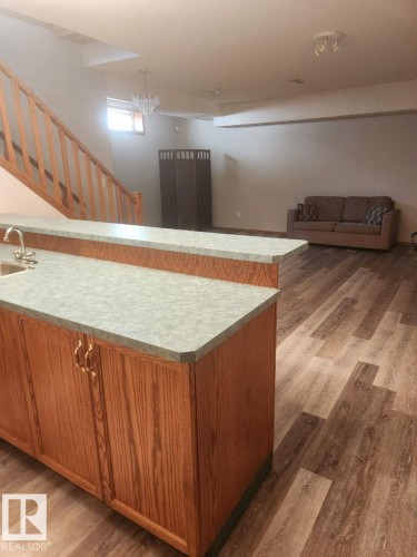 Open-concept basement featuring wood-finish flooring, a built-in wet bar with a stainless steel sink, and a wooden staircase with a banister - 49 Heritage Drive, St. Albert, AB 