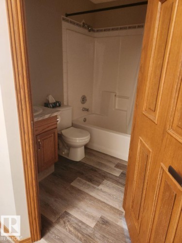 Bathroom with wood-finish flooring, a white bathtub and shower surround, and a wood vanity with a light-colored countertop - 49 Heritage Drive, St. Albert, AB 
