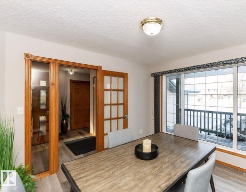 Dining area with wood-finish flooring, a large window with sliding door access, and a wood-framed glass-paneled door - 49 Heritage Drive, St. Albert, AB 