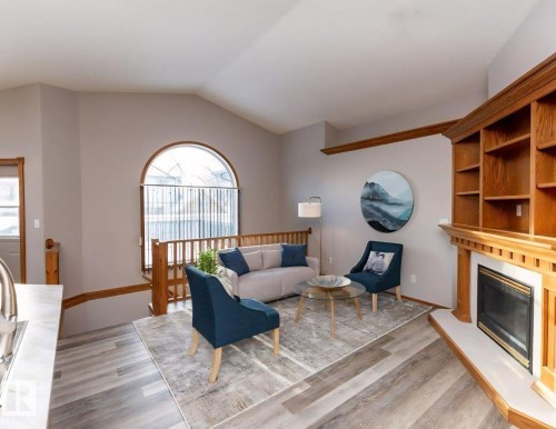 Vaulted ceiling living area featuring wood-finish flooring, an arched window, and a built-in fireplace with shelving - 49 Heritage Drive, St. Albert, AB 