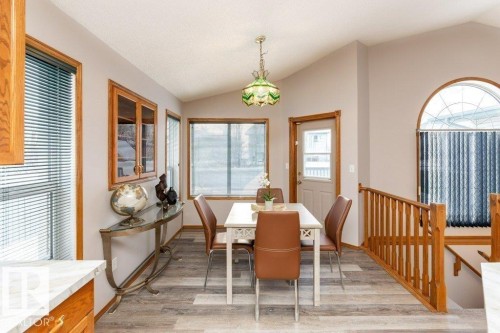 Vaulted ceiling dining area featuring wood-finish flooring, multiple windows with blinds, built-in display cabinetry, and a wood railing - 49 Heritage Drive, St. Albert, AB 