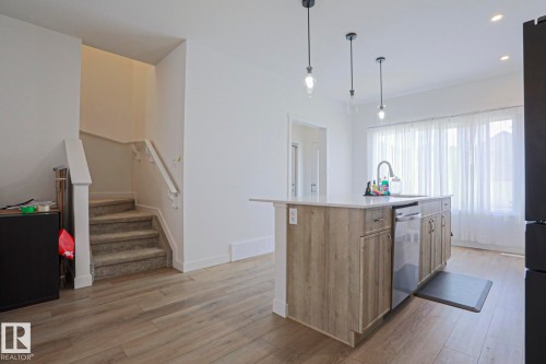 Kitchen island featuring a sink with a gooseneck faucet, integrated dishwasher, and wood-finish cabinetry - 33 Eton Link, Spruce Grove, AB 
