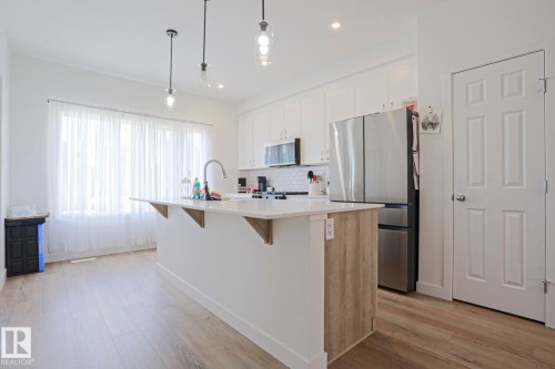 Kitchen featuring a central island with a quartz countertop, wood-finish paneling, and an undermount sink with a gooseneck faucet - 33 Eton Link, Spruce Grove, AB 